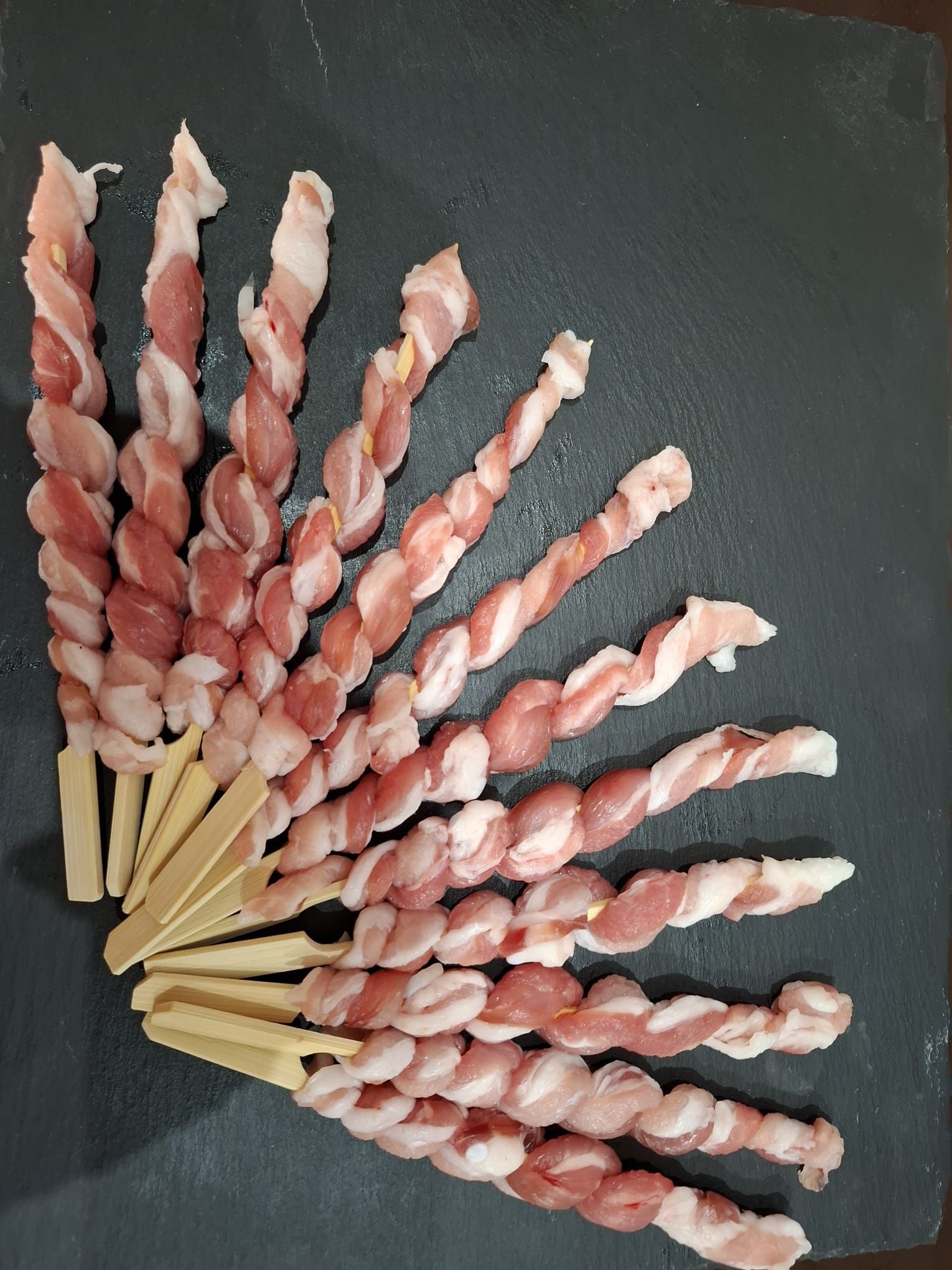 Disposizione a ventaglio di spiedini di pesce rosa e bianchi su una superficie scura
