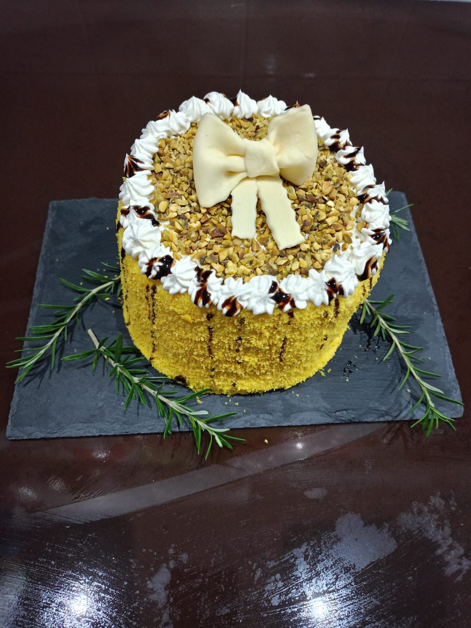 Torta rotonda glassata con decorazione a fiocco di crema su un vassoio di ardesia, decorata con erbe aromatiche e zucchero a velo.