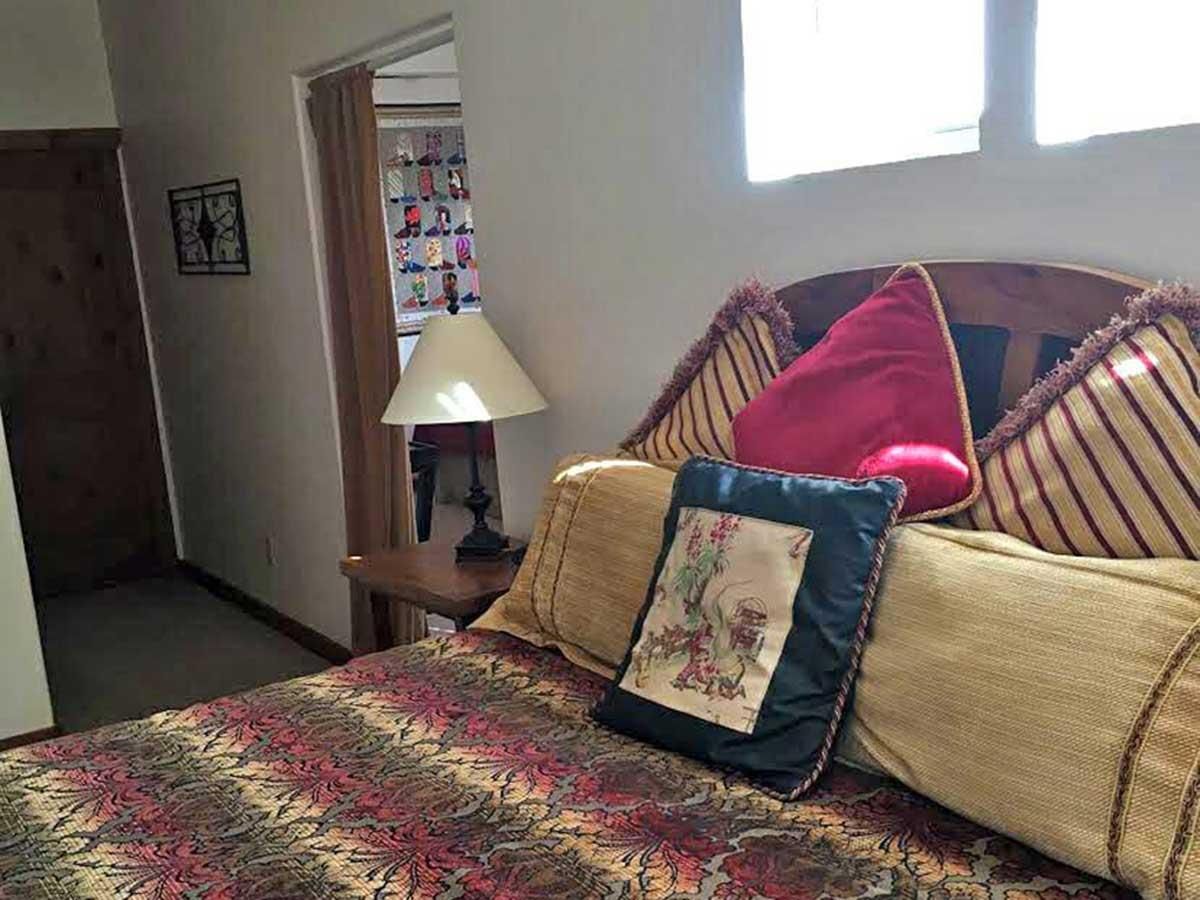 A bedroom with a patterned bedspread, several decorative pillows, and a bedside lamp next to an open doorway.