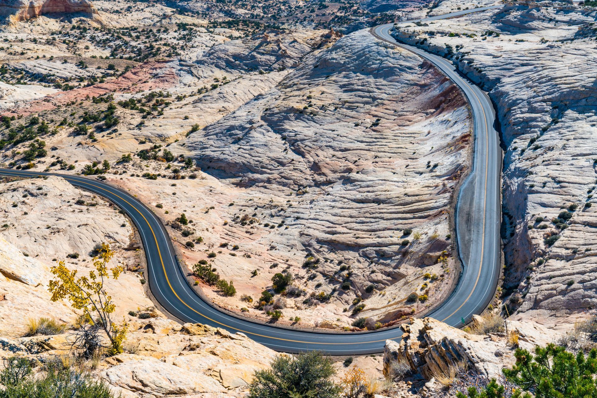 A winding paved road snakes through a rocky, tan-colored desert canyon landscape.