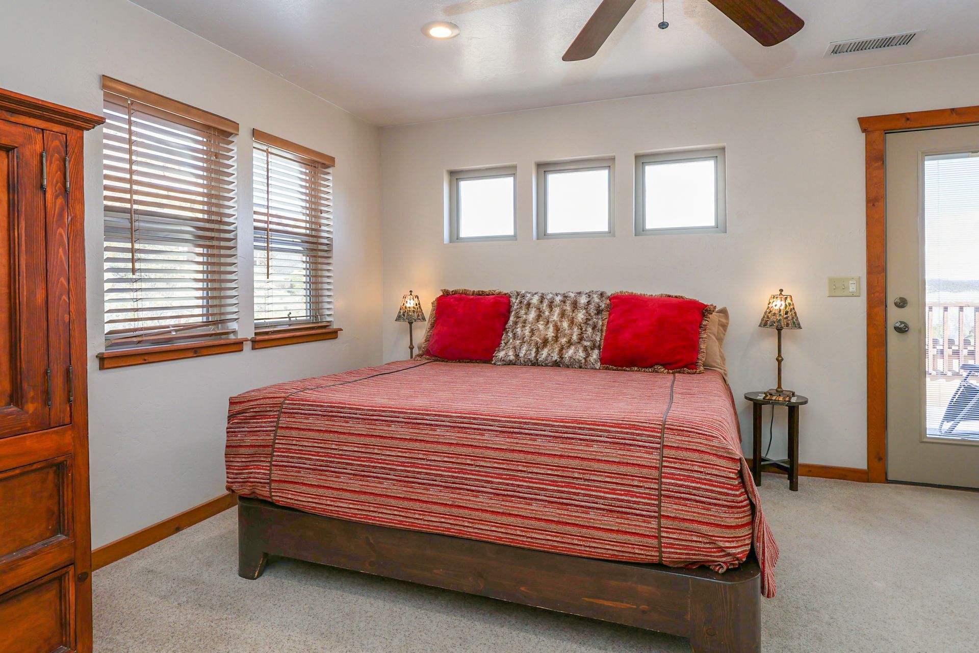 A cozy bedroom with a bed featuring a patterned red cover, two red pillows, a wooden frame, and matching bedside lamps.