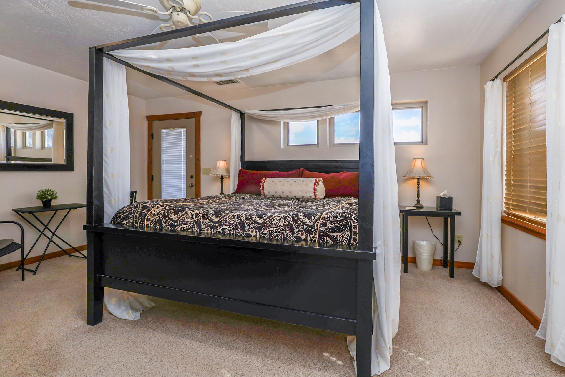 A bedroom features a black canopy bed with sheer white drapes, a patterned comforter, and two side tables with lamps.
