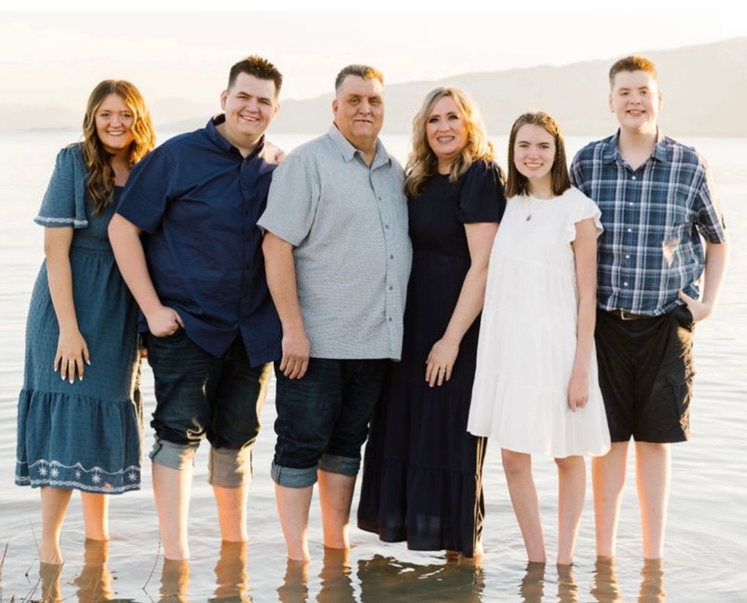 A family of six stands together in shallow water at sunset, posing for a portrait outdoors.