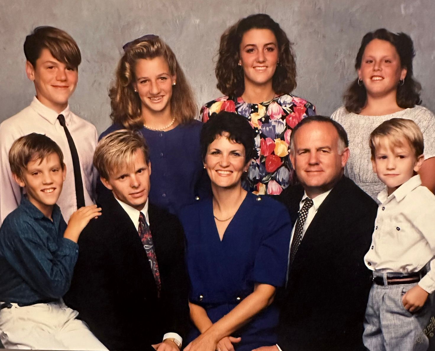 Family portrait of seven people posed in two rows, dressed in formal clothing against a studio backdrop