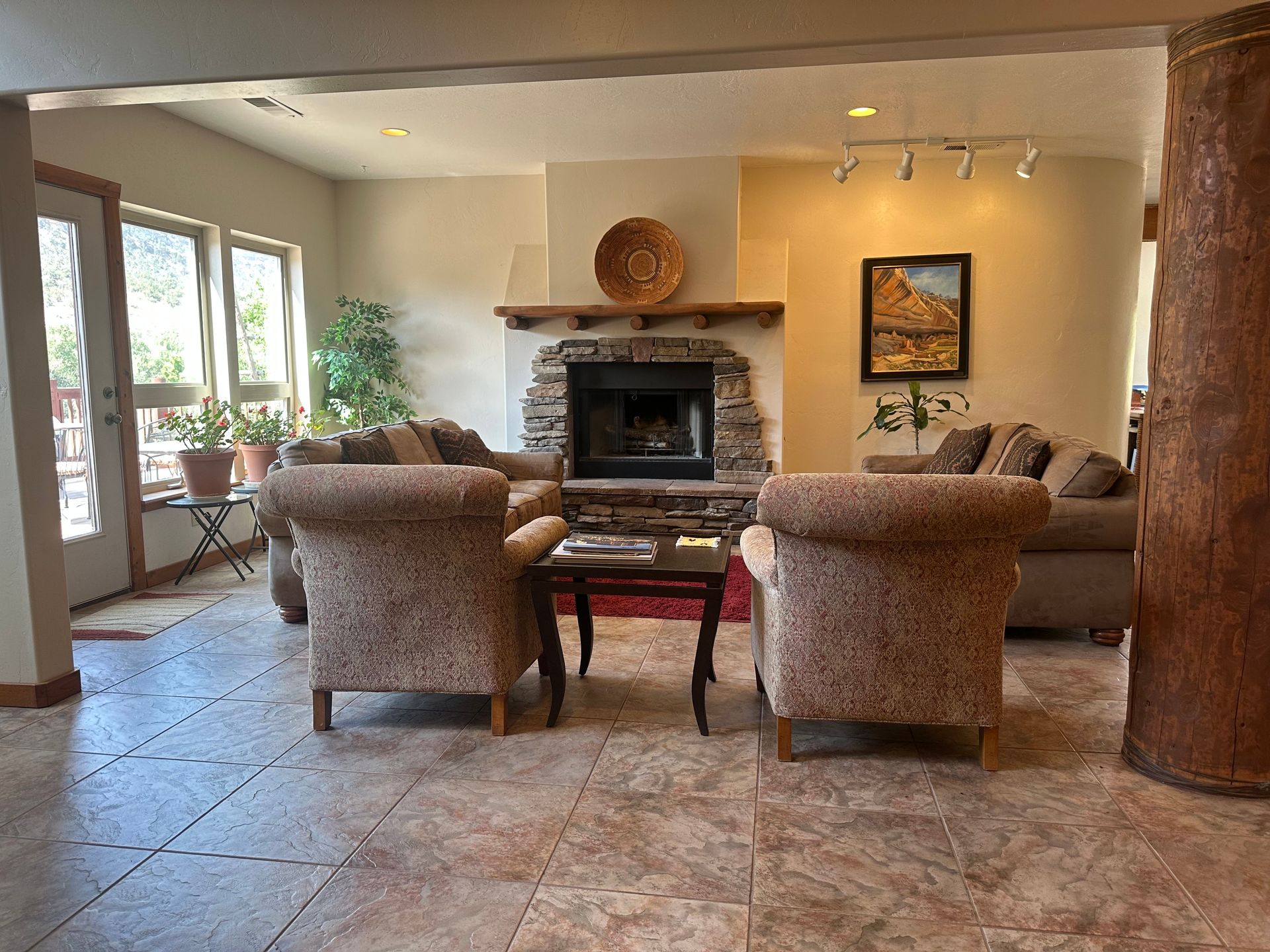 A living room with tile floors, two upholstered armchairs, a stone fireplace, and a large wooden pillar.