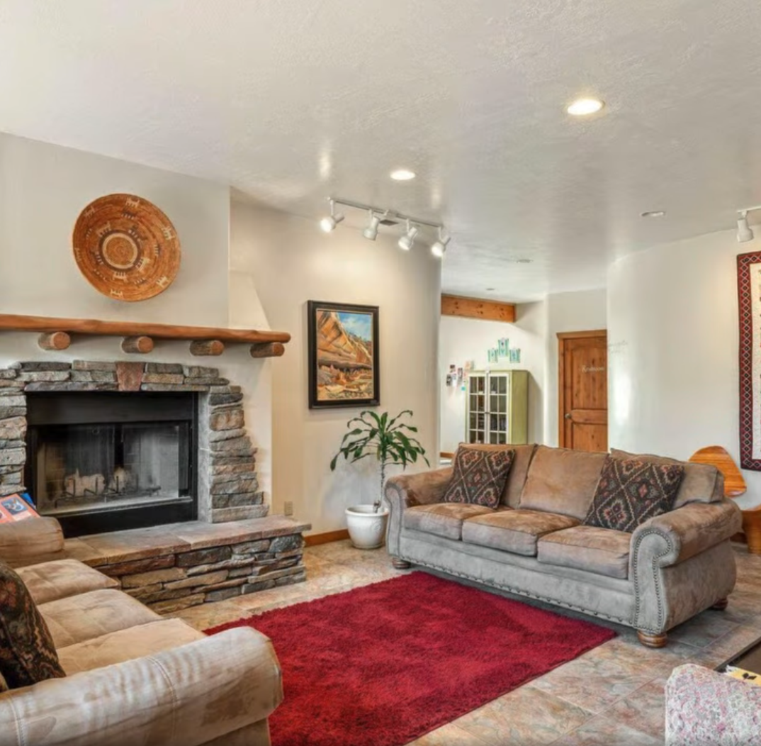 A living room with two brown sofas facing each other on a red rug, centered around a stone fireplace and artwork.
