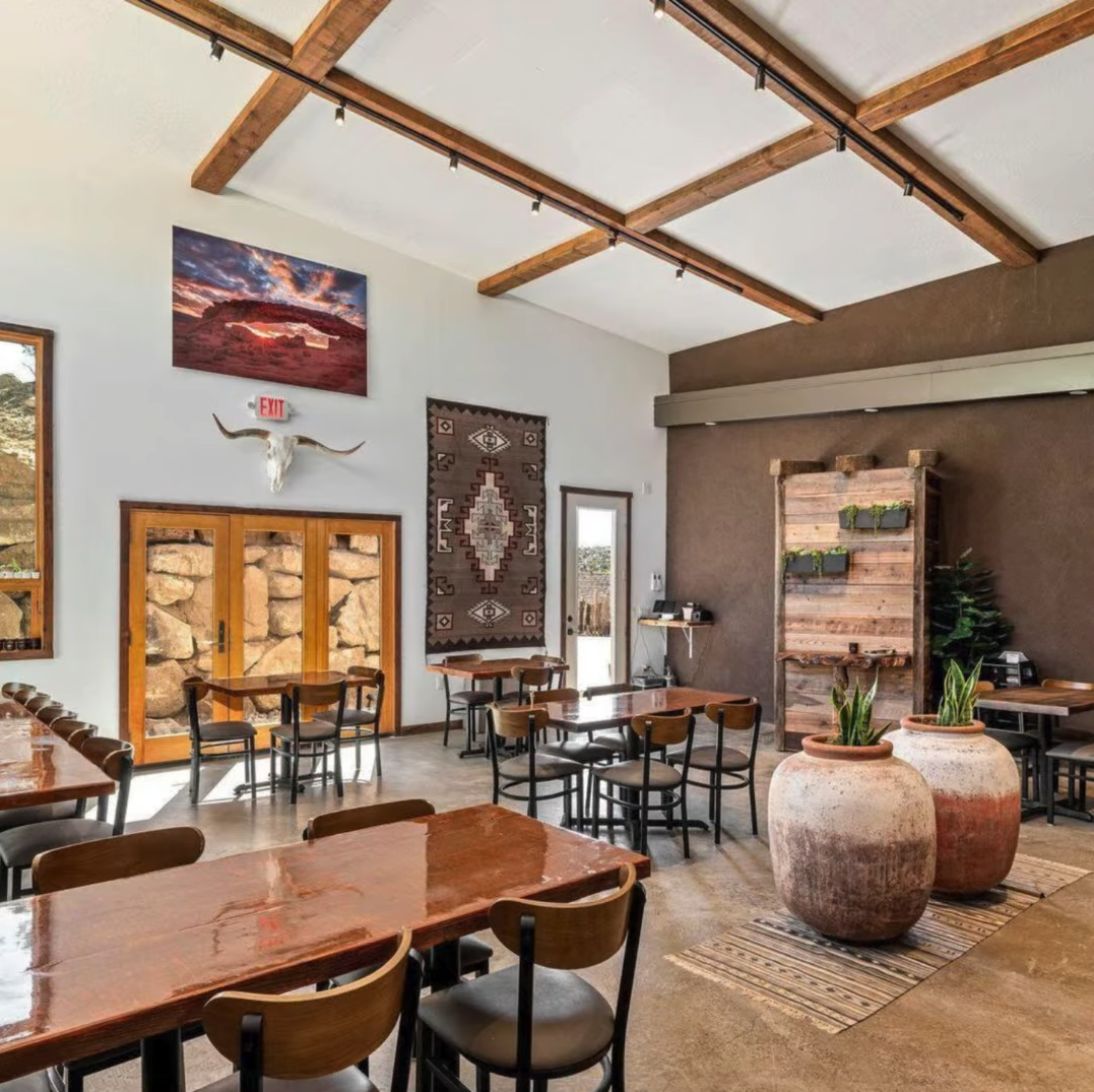 Spacious rustic restaurant dining room with wooden beams, tables, chairs, Native American decor, and large clay planters.