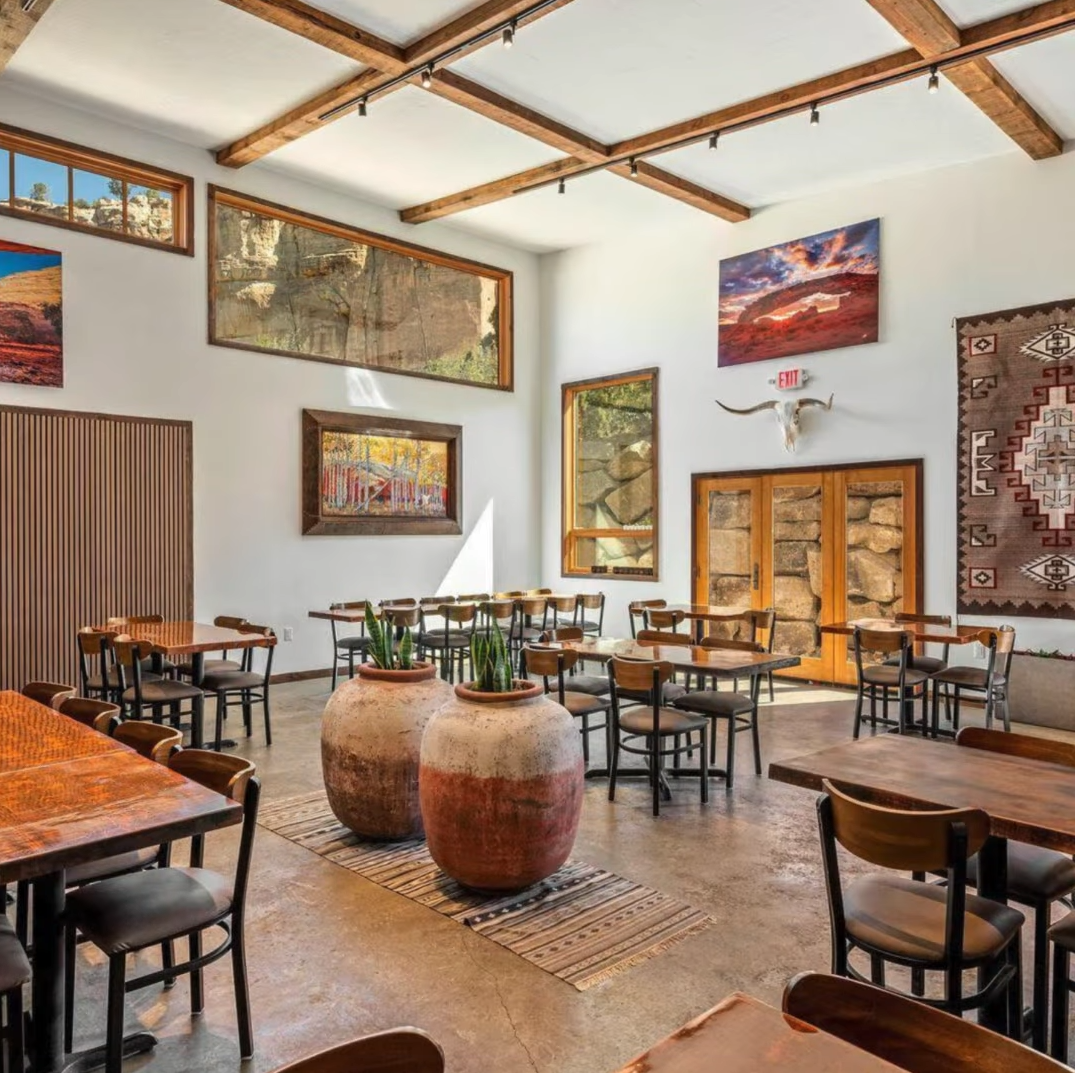 A dining room with rustic decor, wooden tables, chairs, large clay pots, and southwest-style art on the white walls.