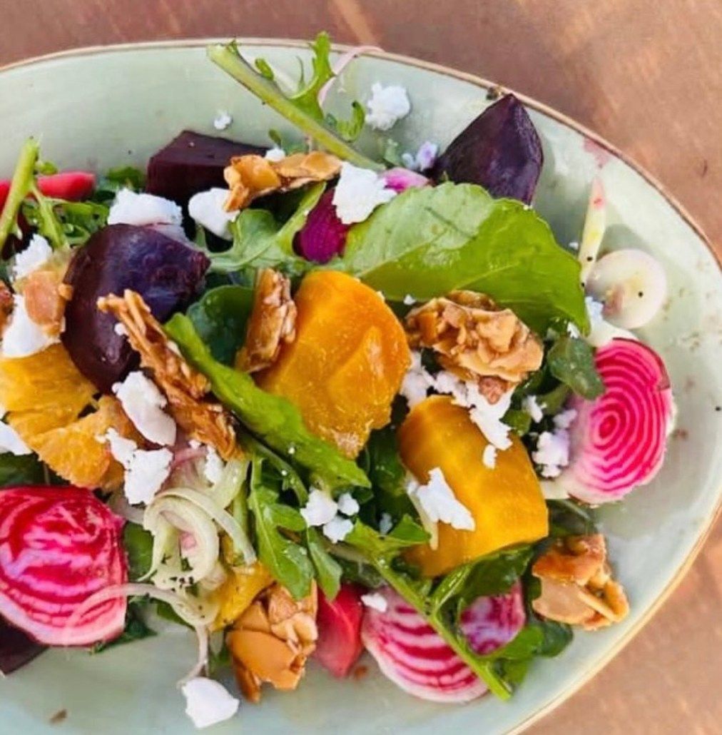 A vibrant salad with roasted red and yellow beets, candy cane beet slices, goat cheese crumbles, and nuts on a plate.