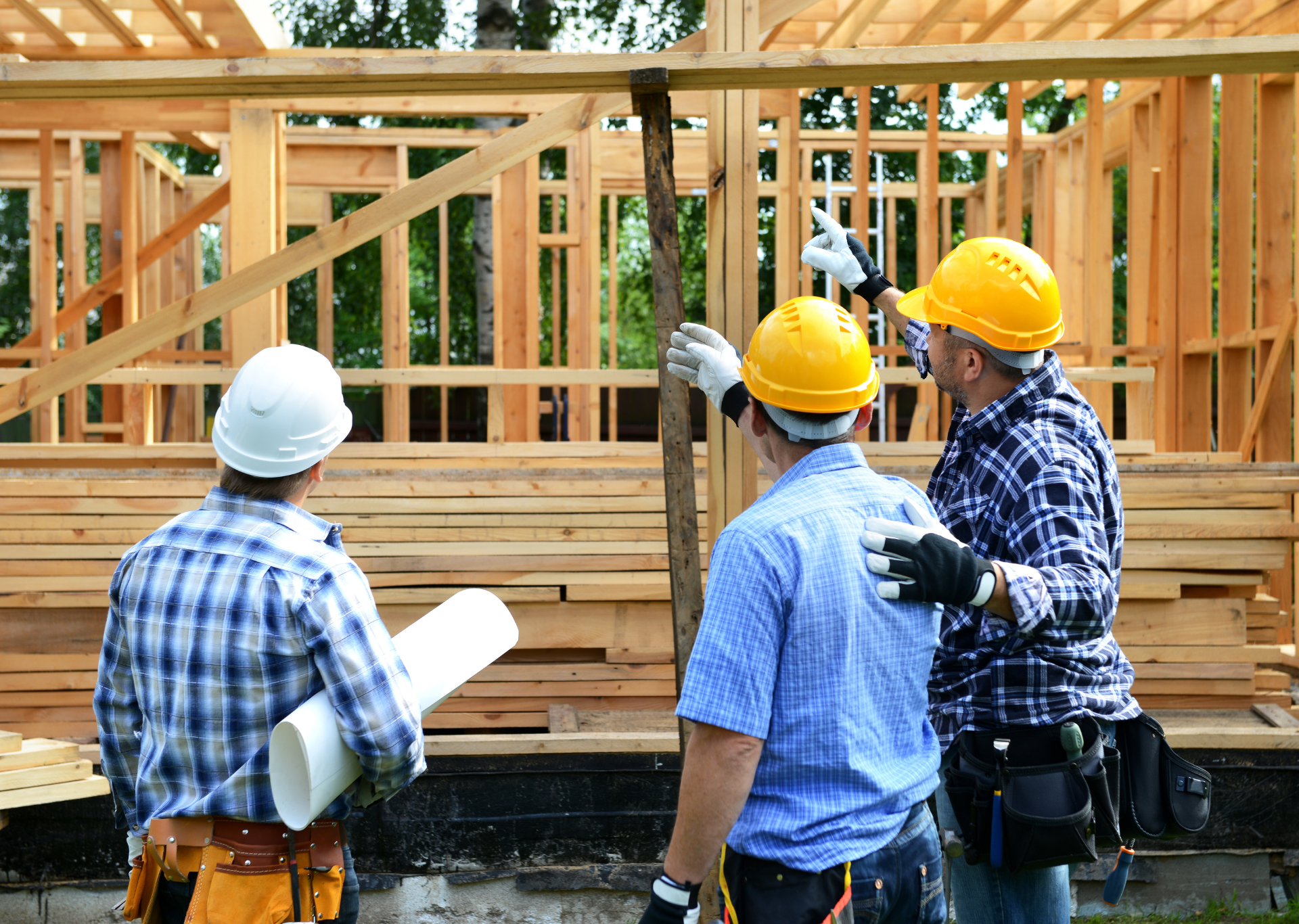 Three construction workers examine wooden framing; two point upward, all wearing hard hats.