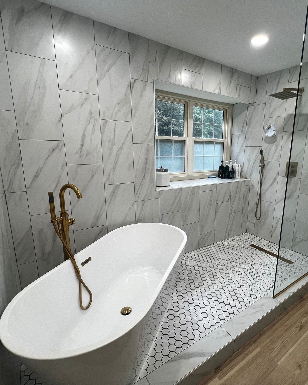Bathroom with a white tub and marble tiled walls, gold faucet, and shower with glass door.