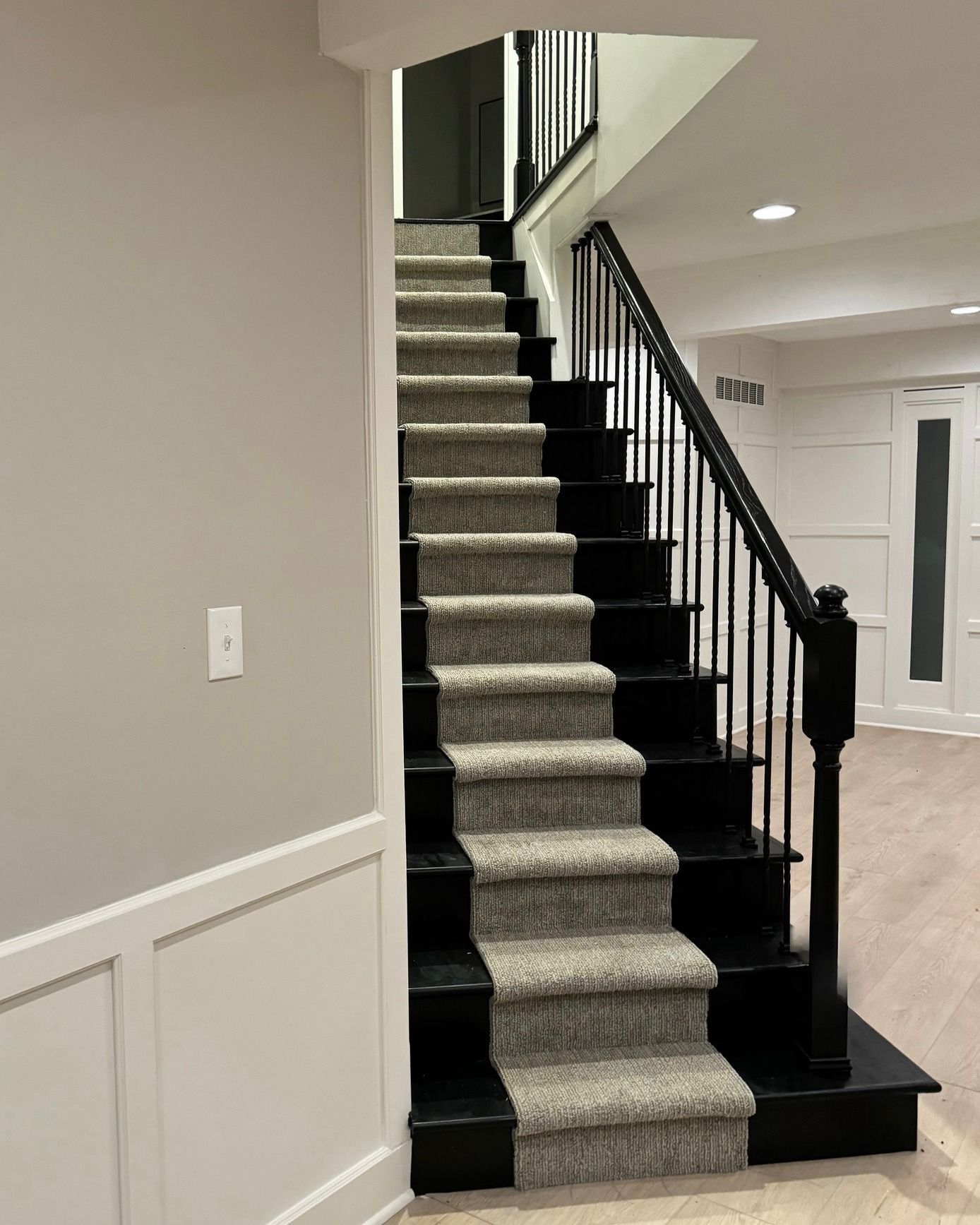Staircase with carpeted runner on steps, black risers and railing, in a basement setting.