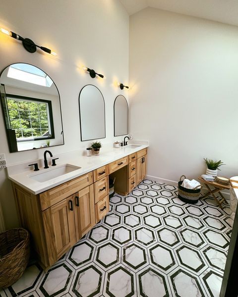 Bathroom with light wood vanity, arched mirrors, black hardware, and hexagon tile floor.