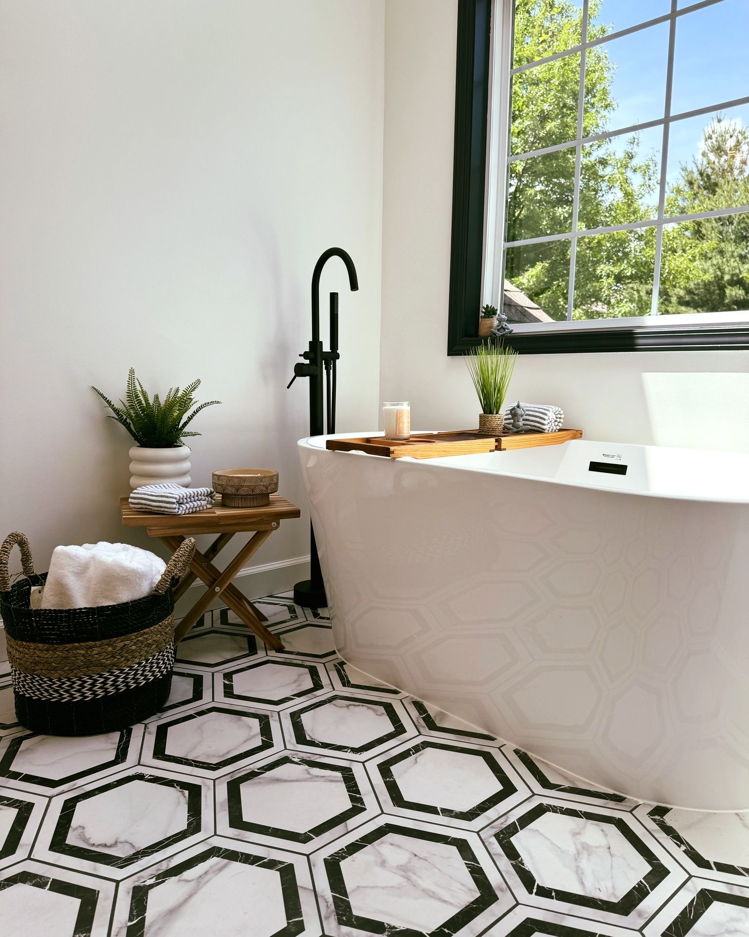 Modern bathroom with hexagonal tile floor, white tub, black faucet, and large window with view.
