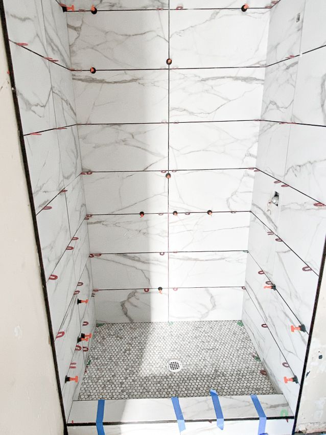 A shower stall with white tiles being installed in a bathroom.