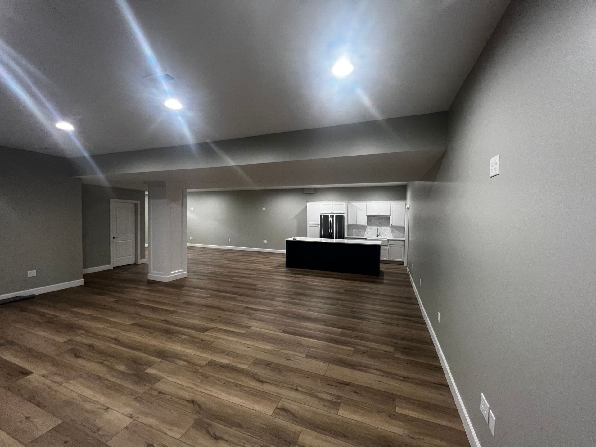 Empty finished basement with kitchen, wood floors, and gray walls.