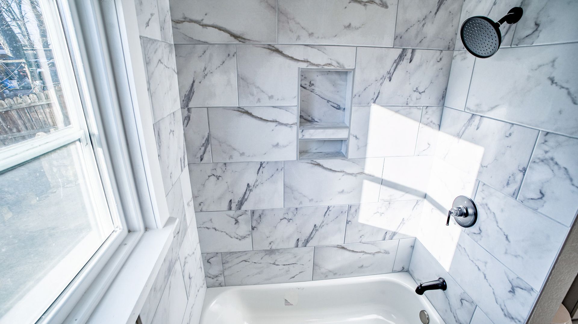 A bathroom with marble tiles , a tub , a shower and a window.