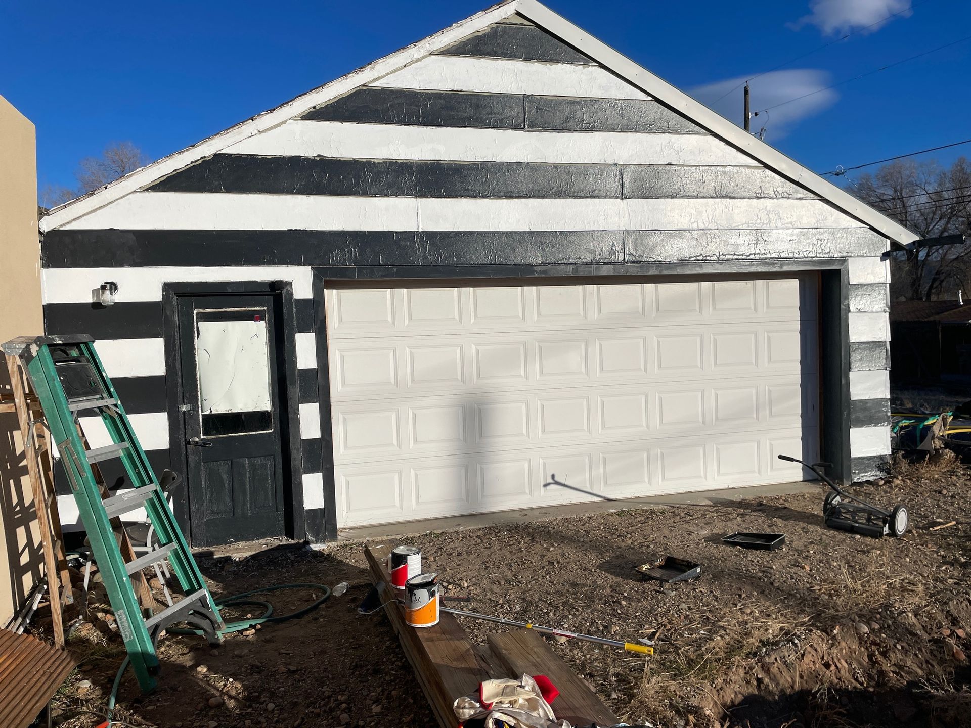 Garage painted black and white, with door, closed garage door, and ladder.