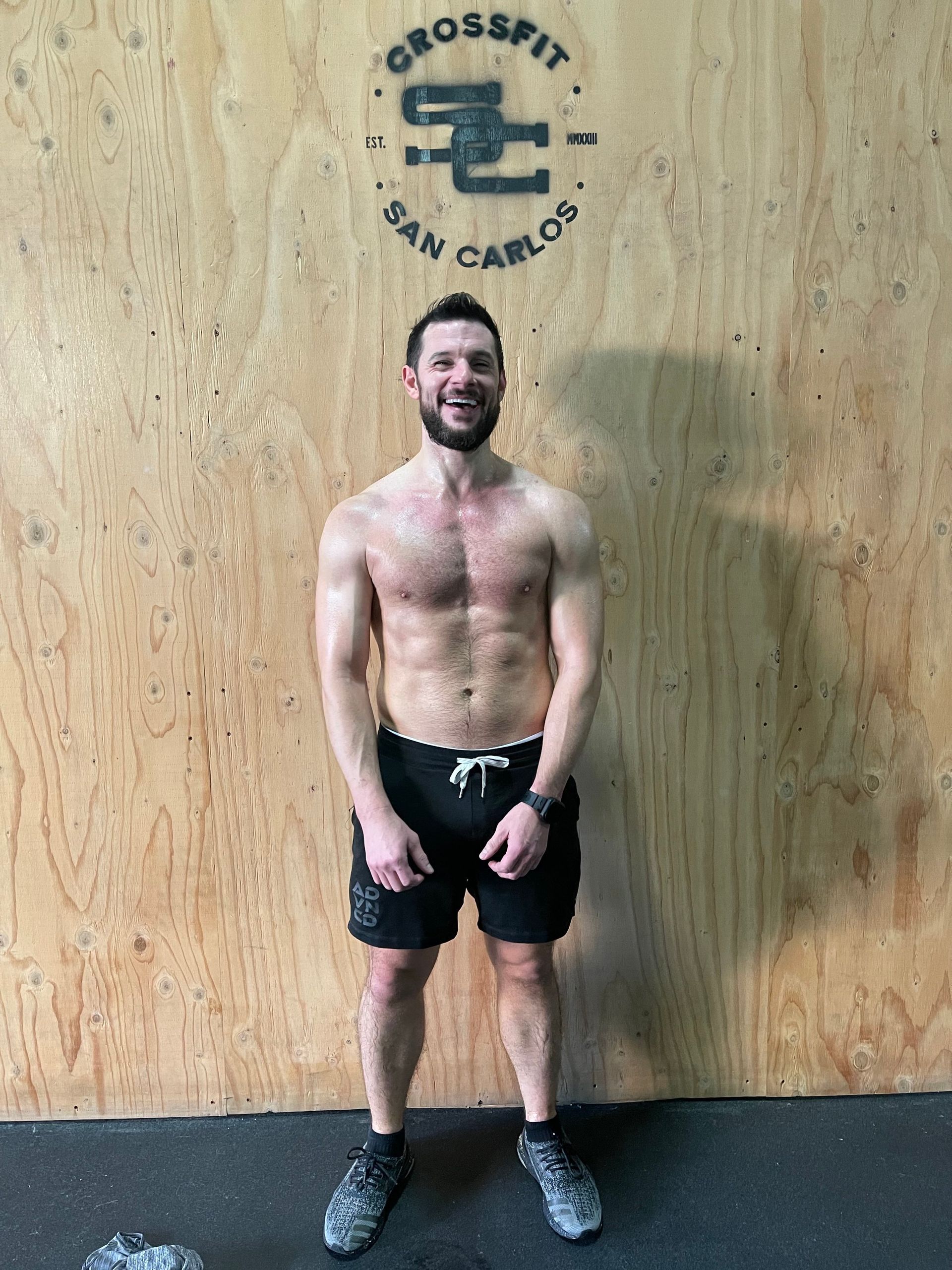 A shirtless man is standing in front of a wooden wall.