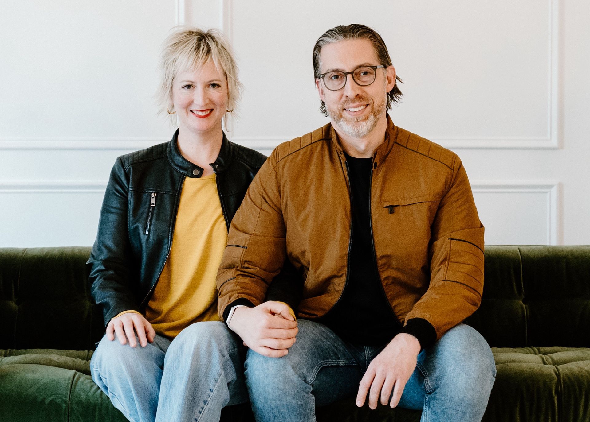 A man wearing a blue shirt that says love is blinds is standing in front of a brick wall.