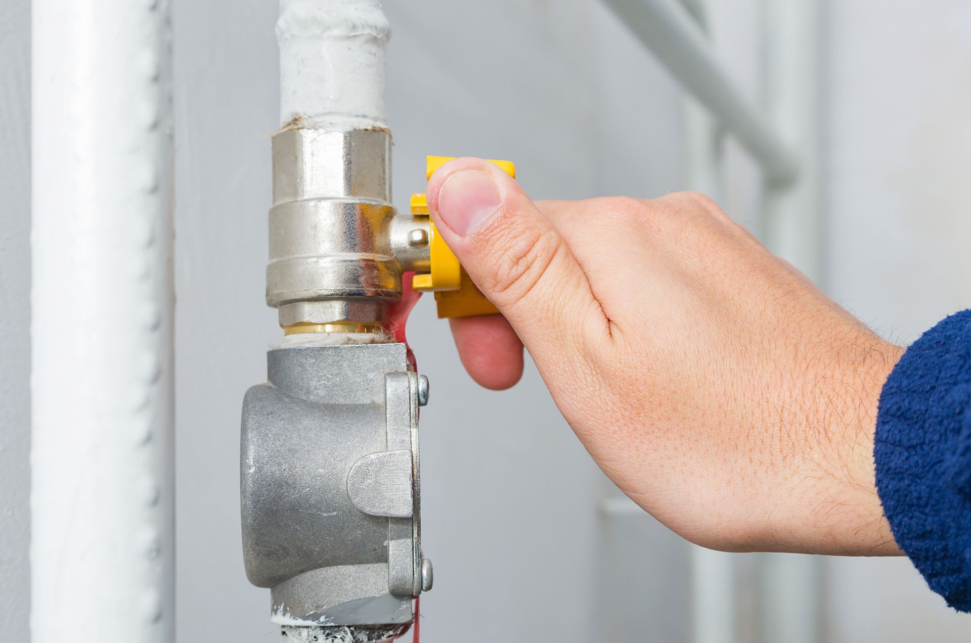 Close-up of hand closing a gas valve inside a broiler room, with a blurry background.