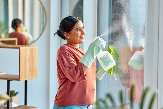 A woman disinfects her windows with an eco-friendly spray cleaner