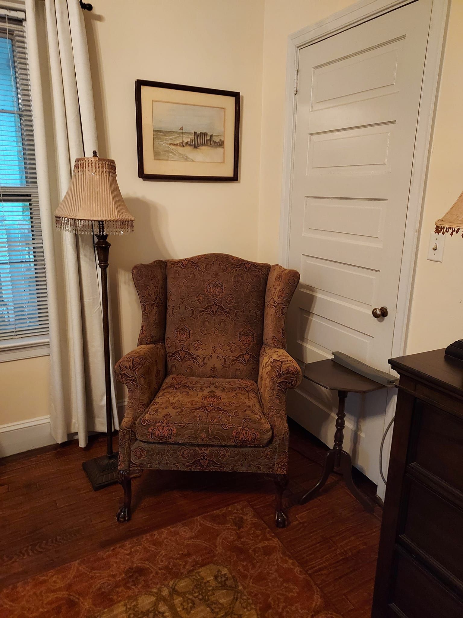 A patterned armchair in a room next to a floor lamp, a small table, and a closed white door.