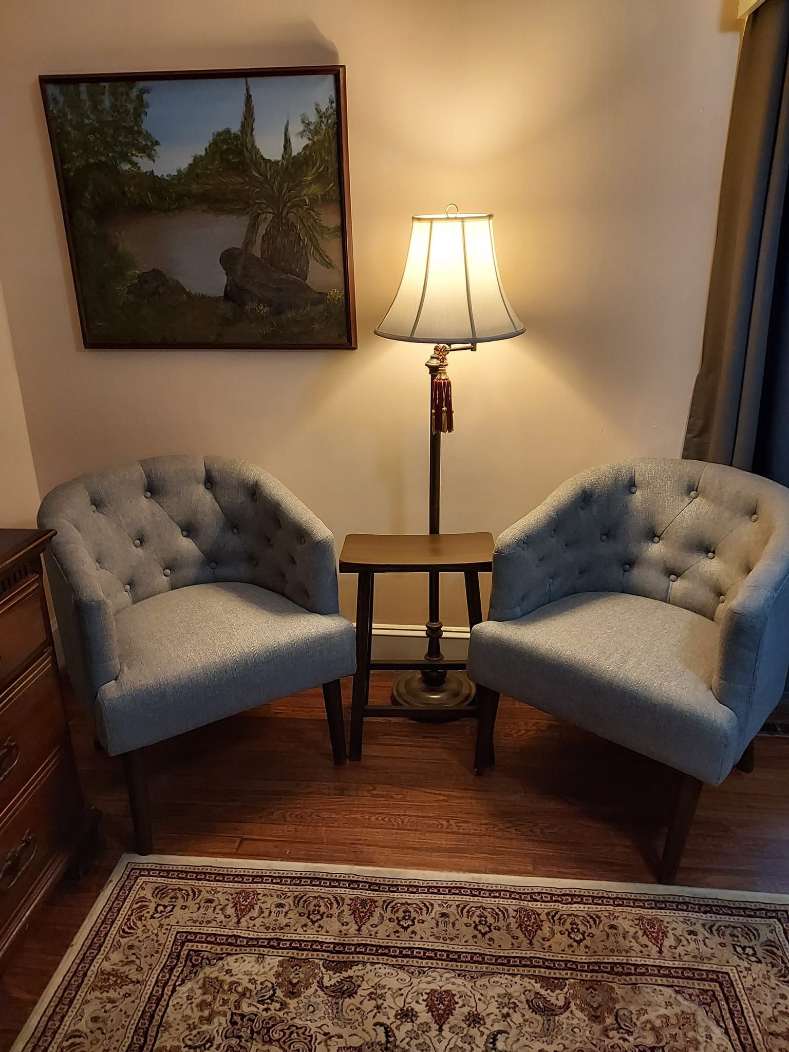 Two gray armchairs face each other, with a lamp and table between them. A painting hangs above.