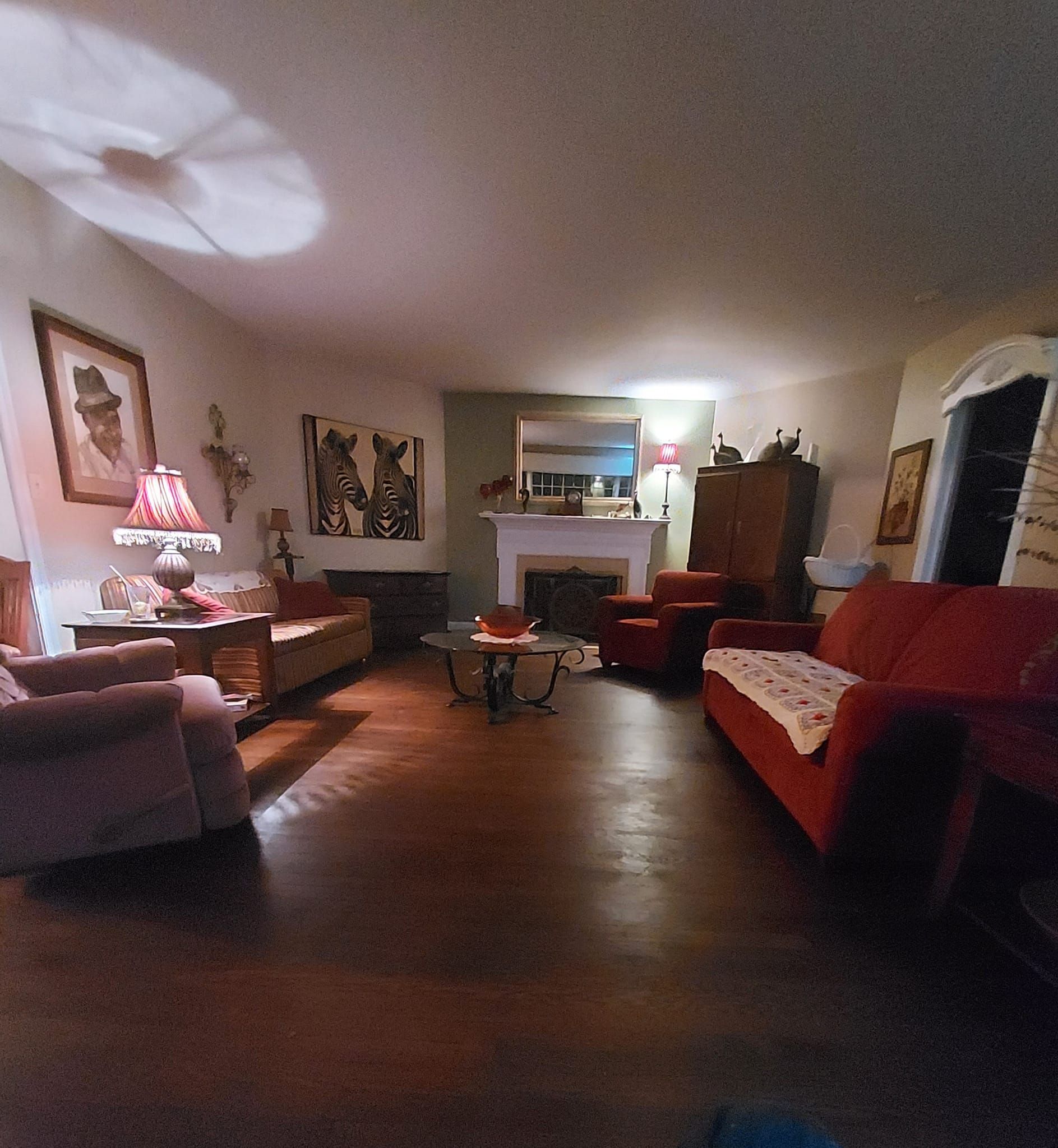 Living room with red couches, fireplace, and various antique furnishings. Dark wood floors, dim lighting.
