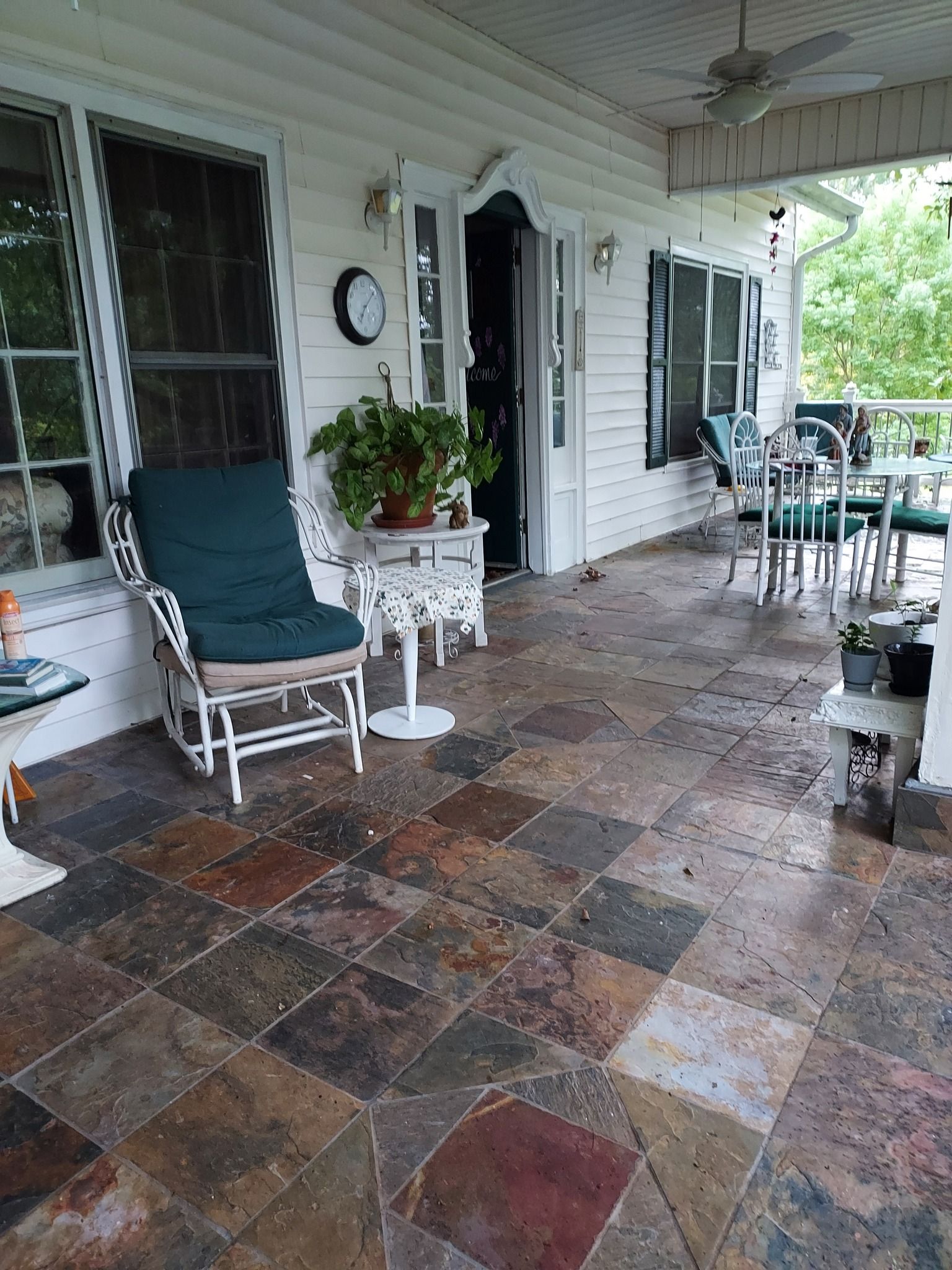 Porch with slate tile flooring, white wicker furniture, and potted plants.