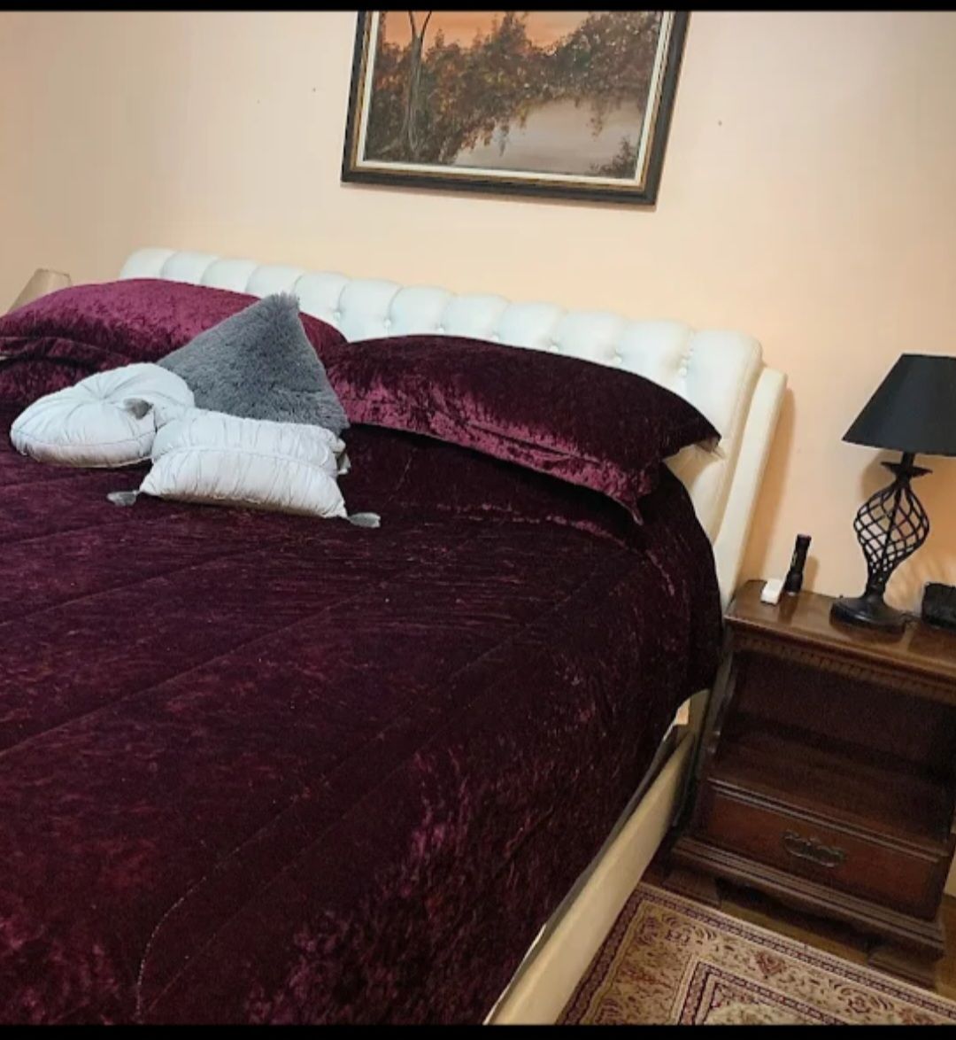 Bedroom with dark wood bed frame, patterned comforter, several decorative pillows, and landscape painting above.