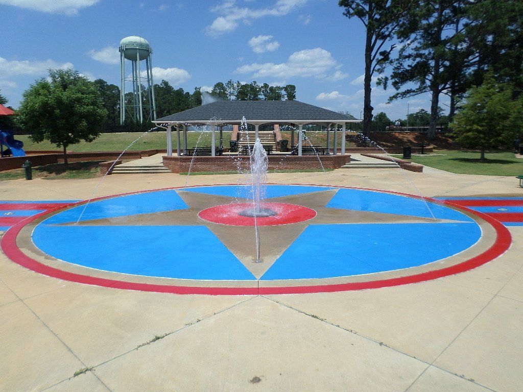 A splash pad with a central fountain, featuring a compass rose design, under a sunny sky.