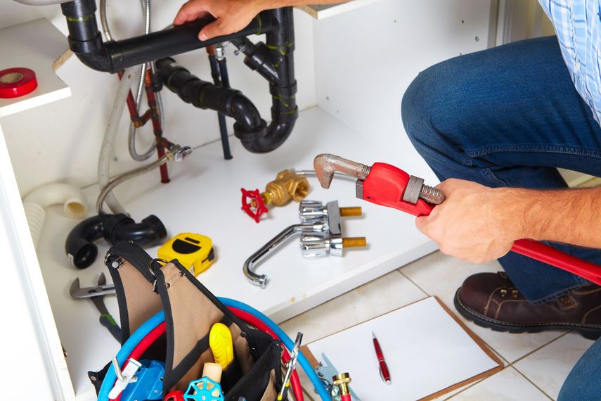 A plumber is working under a sink with a wrench.