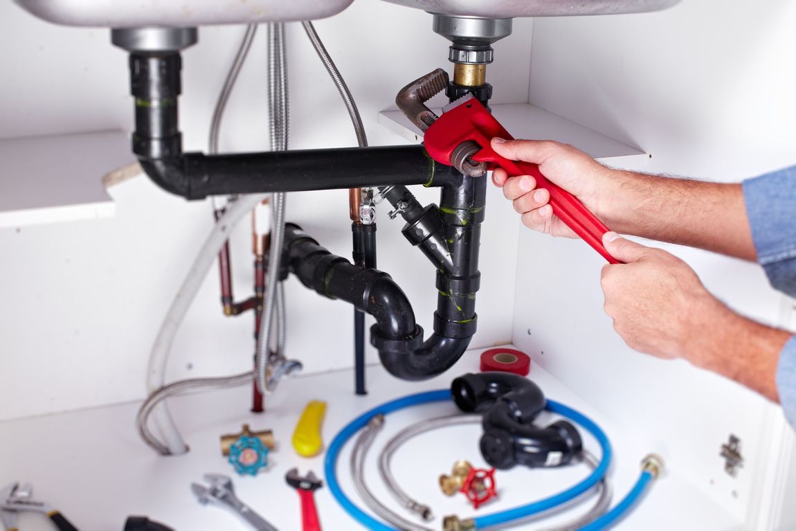 A plumber is fixing a sink with a wrench.