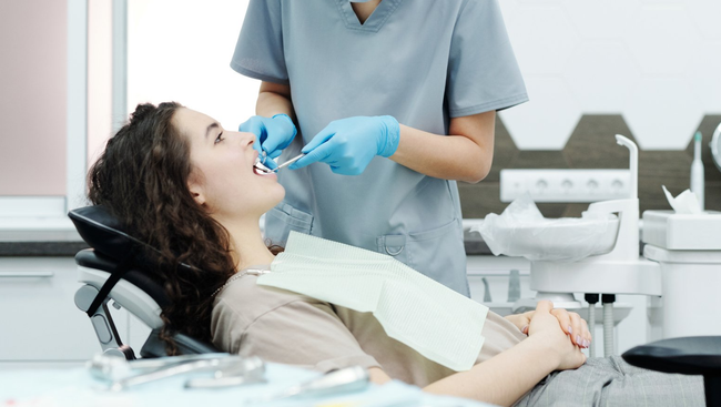 A woman is sitting in a dental chair getting her teeth examined by a dentist.