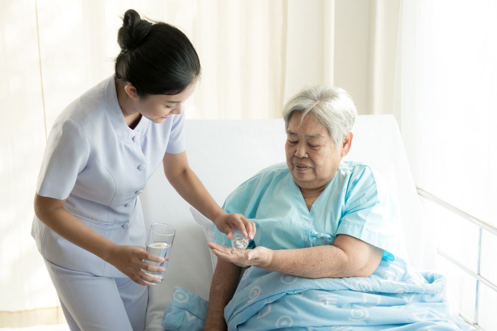 A Nurse Is Giving An Elderly Woman A Pill In A Hospital Bed — NQ Health In Bayview Heights, QLD