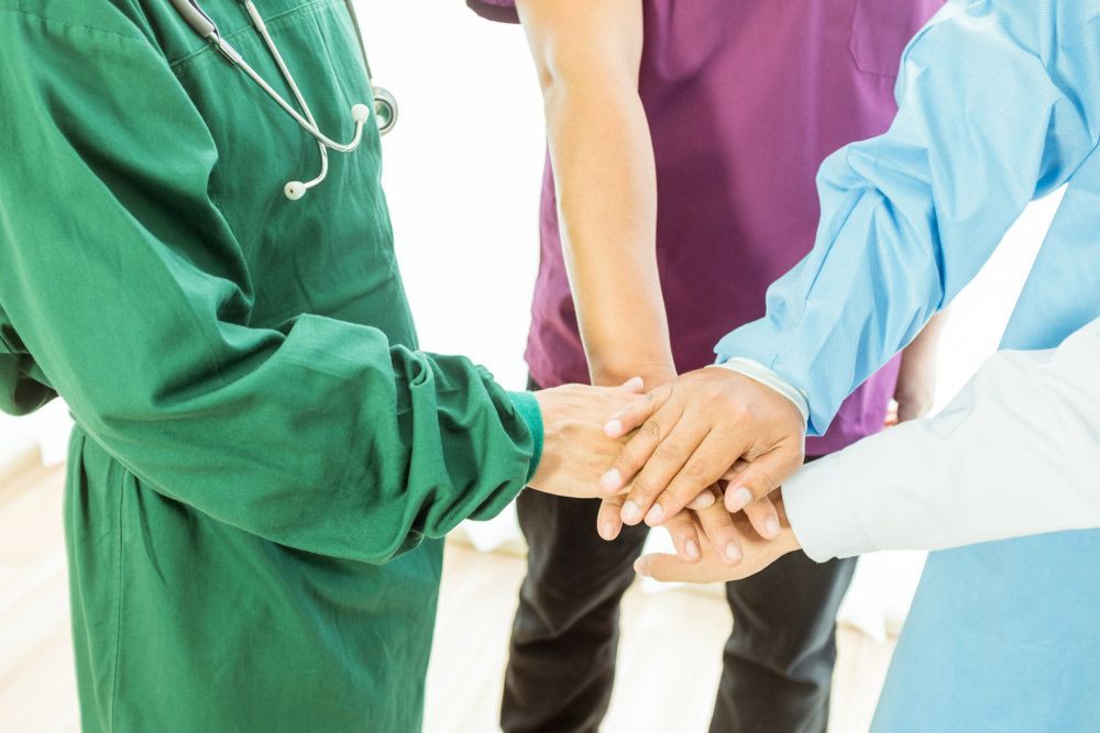 A Group Of Doctors And Nurses Are Putting Their Hands Together — NQ Health In Bayview Heights, QLD