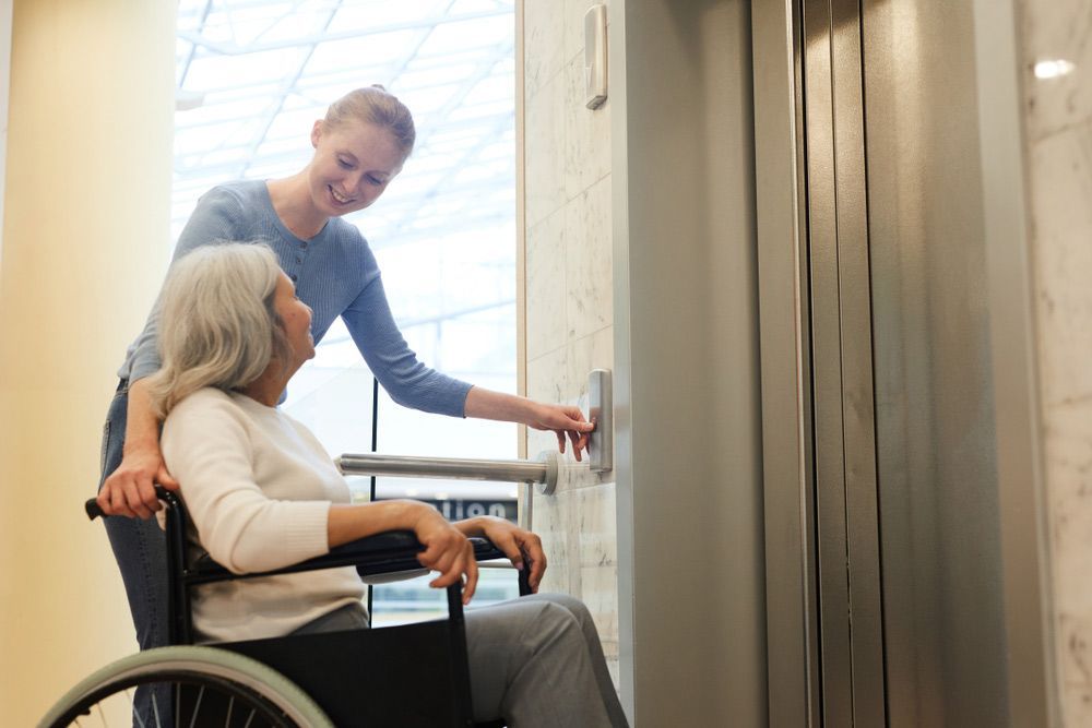 A Woman In A Wheelchair Is Being Helped Into An Elevator By A Nurse — NQ Health In Bayview Heights, QLD