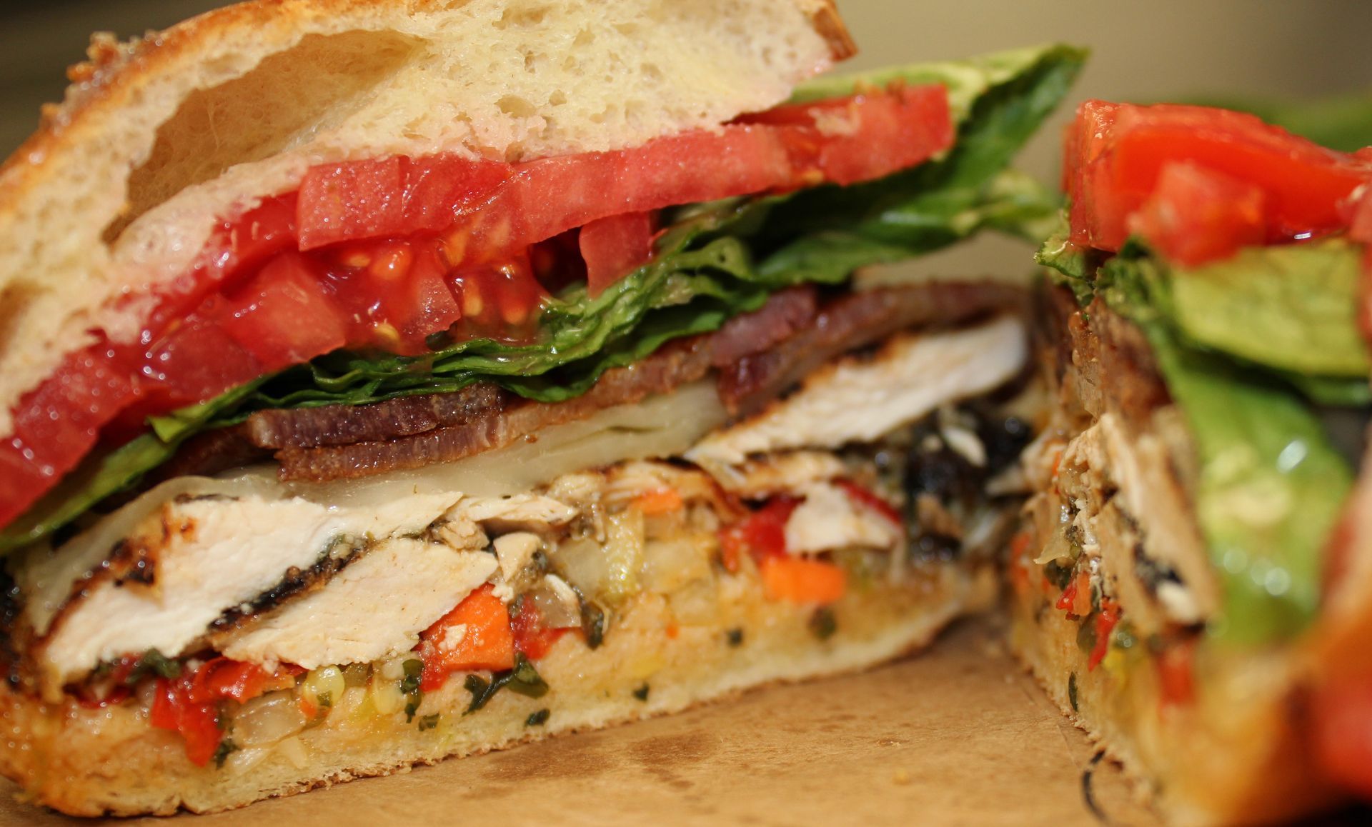 A close up of a sandwich with tomatoes and lettuce on a wooden table.