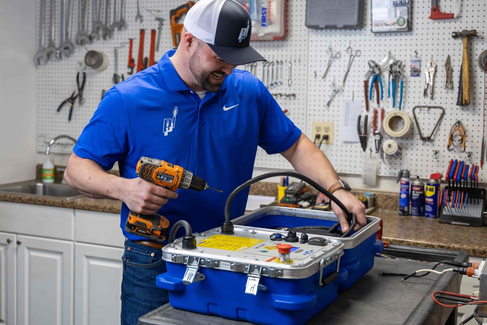 A man is using a drill to fix a machine in a garage.