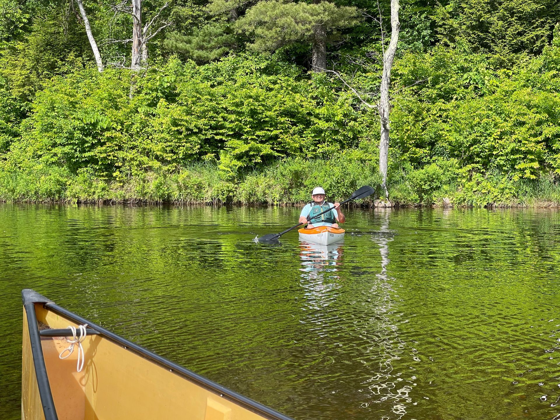 View from a canoe looking toward a man in a kayak on a lake in the Adirondack Park