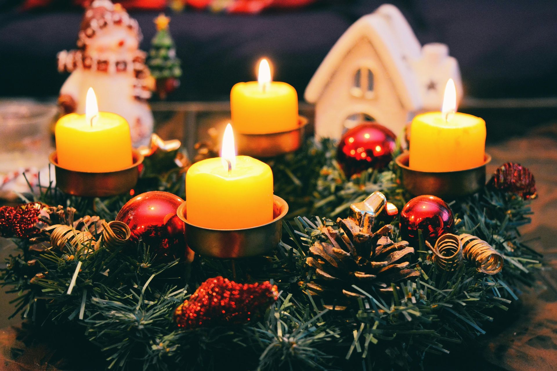Explore the Charm of Our Mountain Village This Winter!  Cozy image of four lit candles in a circular wreath in the foreground with a small snowman and model home in the background.