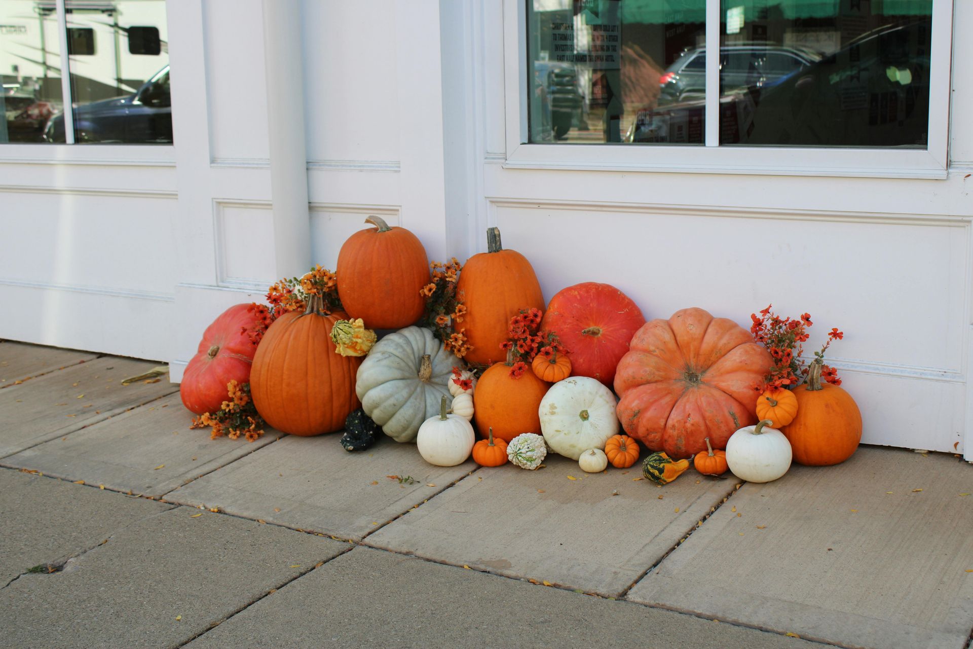 A grouping of multiple colorful pumpkins set in front of a white building