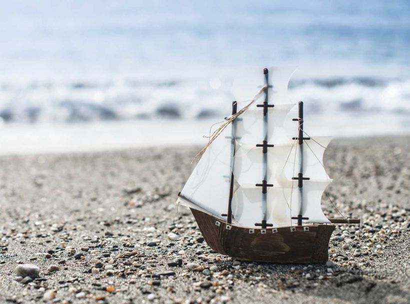 a small model ship sits on a sandy beach near the ocean