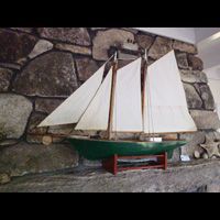 a model sailboat is sitting on a mantle in front of a stone wall .