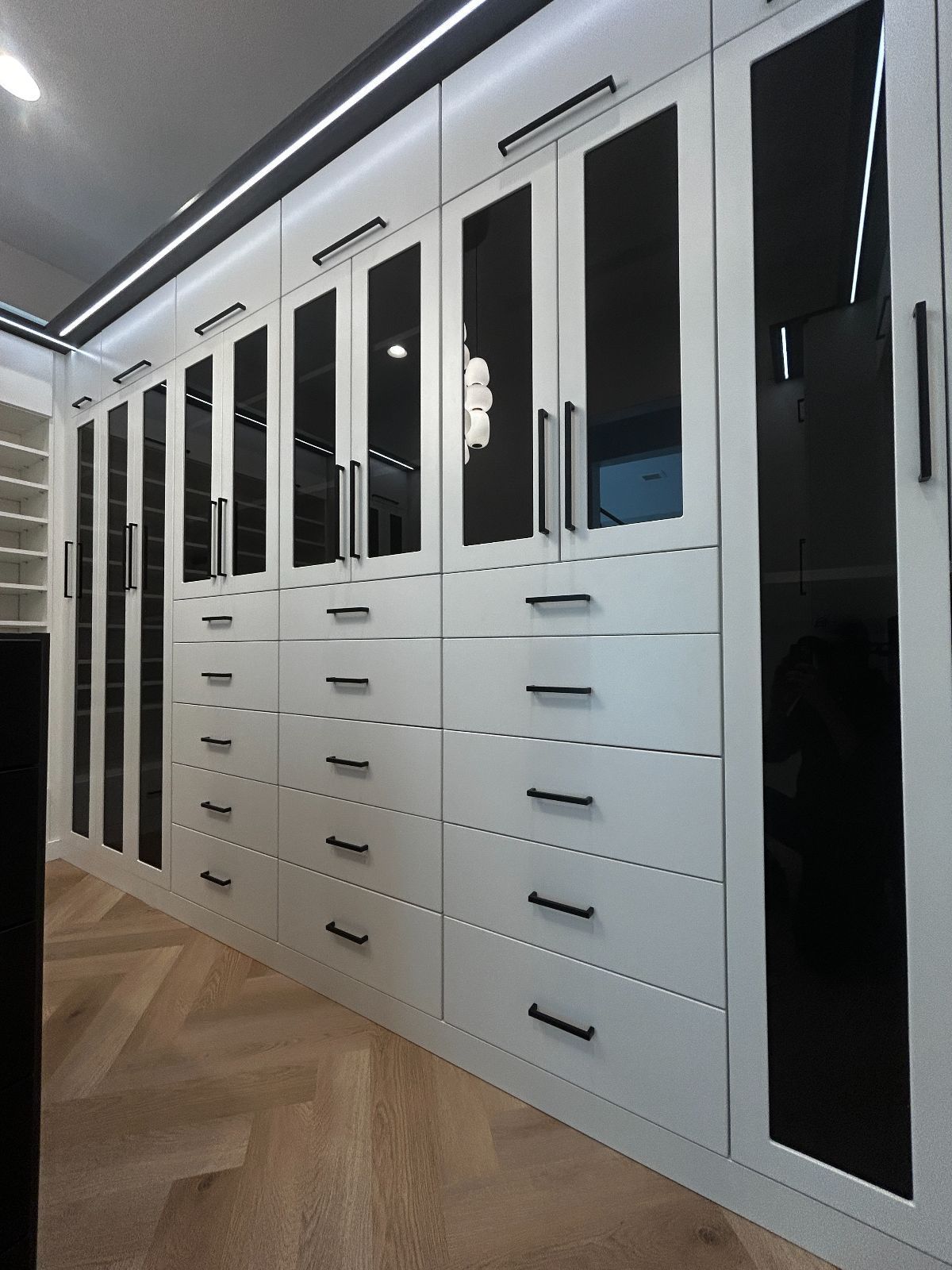 White modern custom closet with black accents and glass doors.