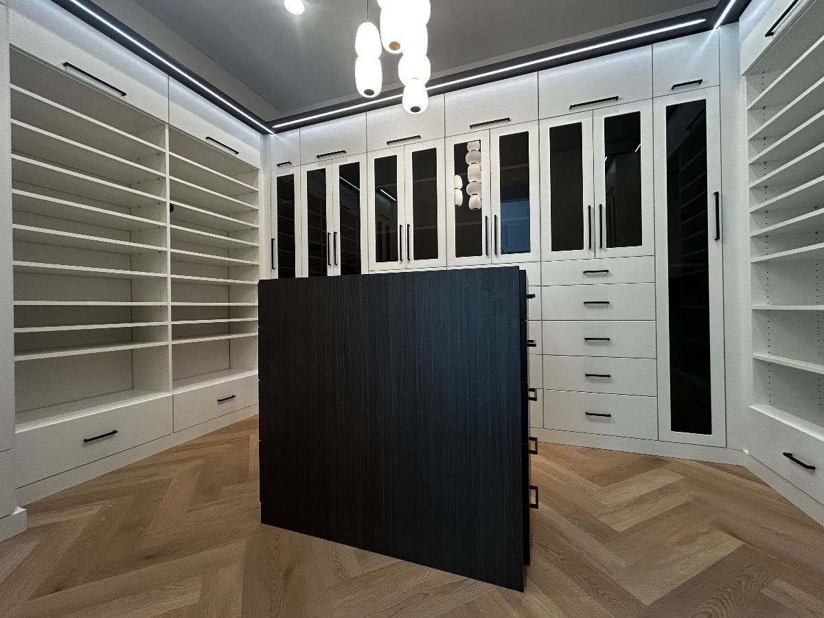 Walk-in closet with white shelving, dark center island, and wood flooring.