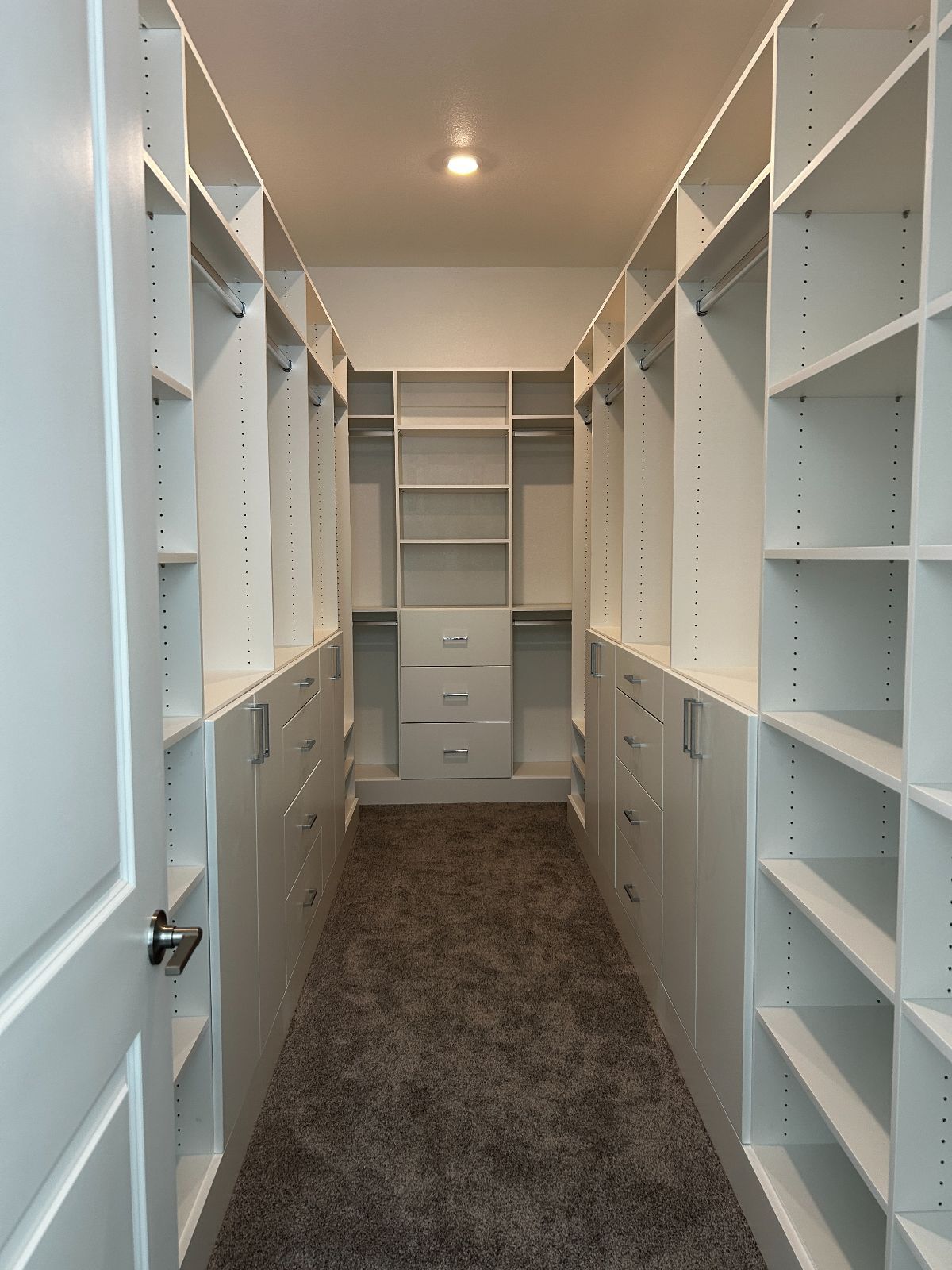 Walk-in closet with white shelving and drawers on both sides, carpeted floor, and central hanging space.