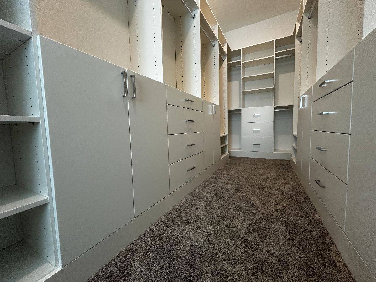 Walk-in closet with white cabinets, shelves, drawers, and carpeted floor.