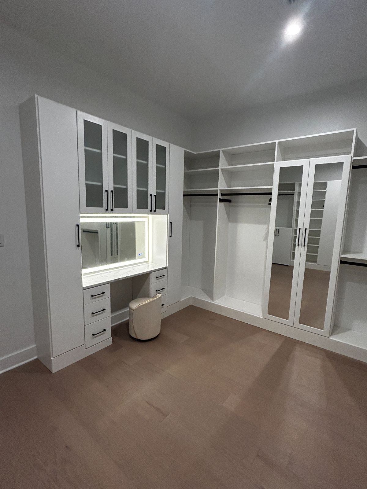 White custom closet with a vanity and a large mirror; tan carpet.
